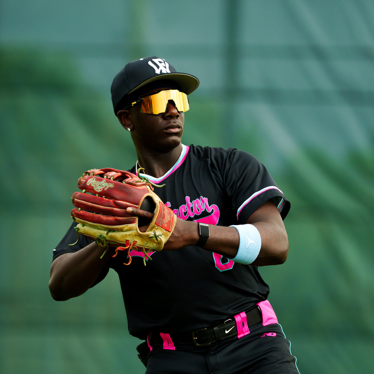 A Person in a black Wow Factor sports uniform with pink accents holding a baseball glove against a green background.
