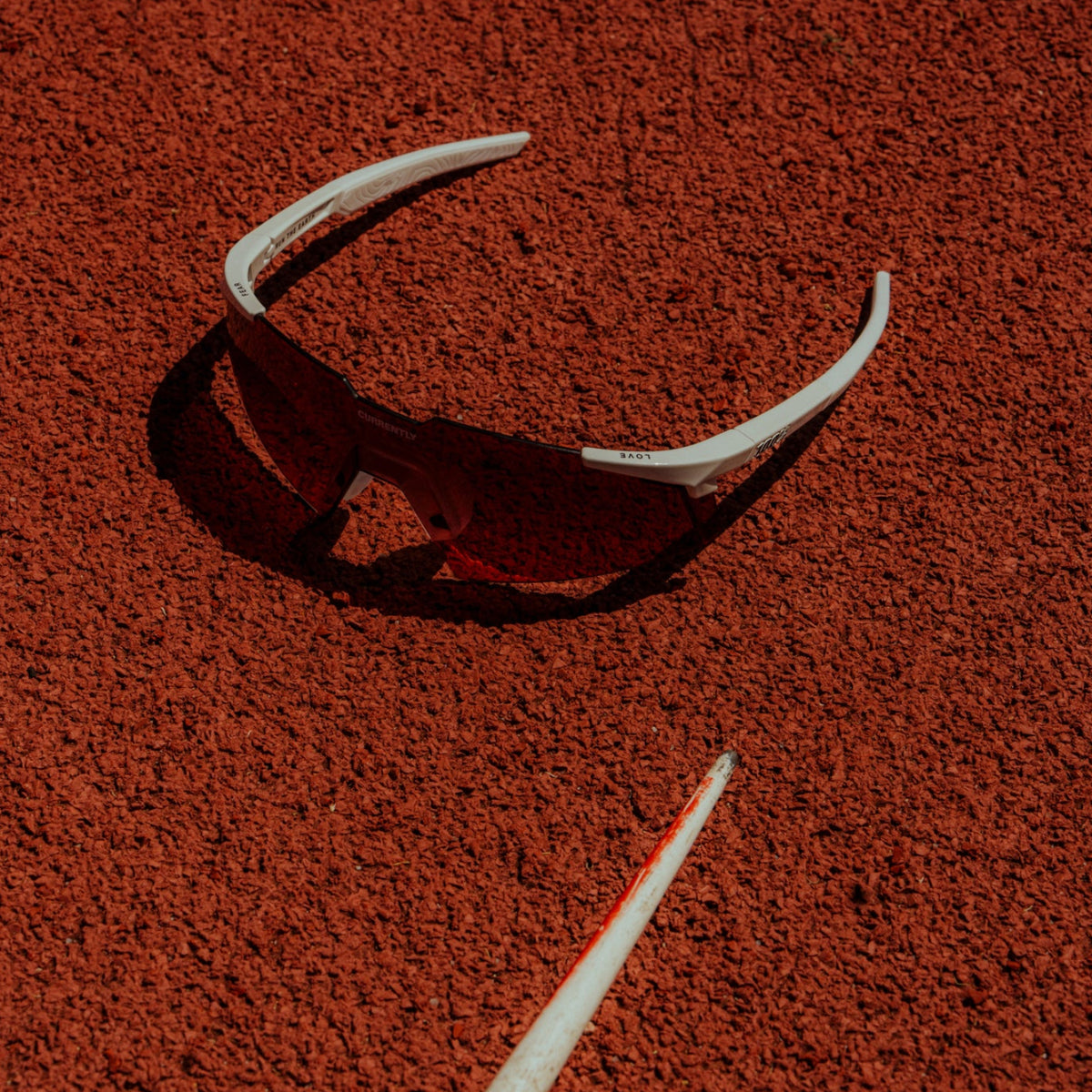 Currently Running™ x 100Percent® Collection - Featuring a lone pair of 100Percent A2 Sunglasses sitting on a red running track.